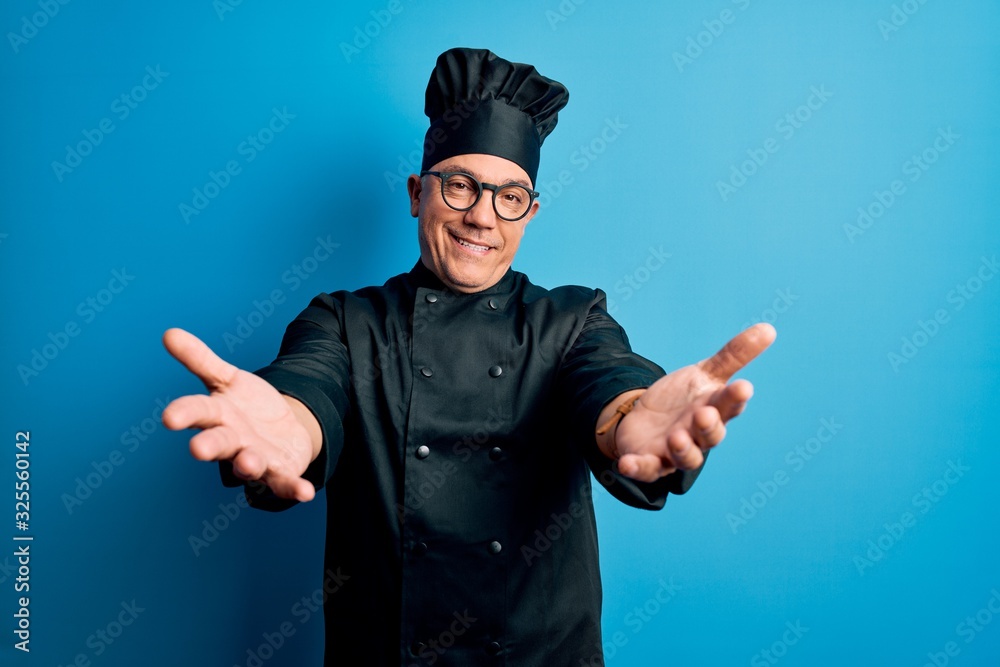Middle age handsome grey-haired chef man wearing cooker uniform and hat smiling cheerful offering hands giving assistance and acceptance. Middle age handsome grey-haired chef man wearing cooker uniform and hat smiling cheerful offering hands giving assistance and acceptance.