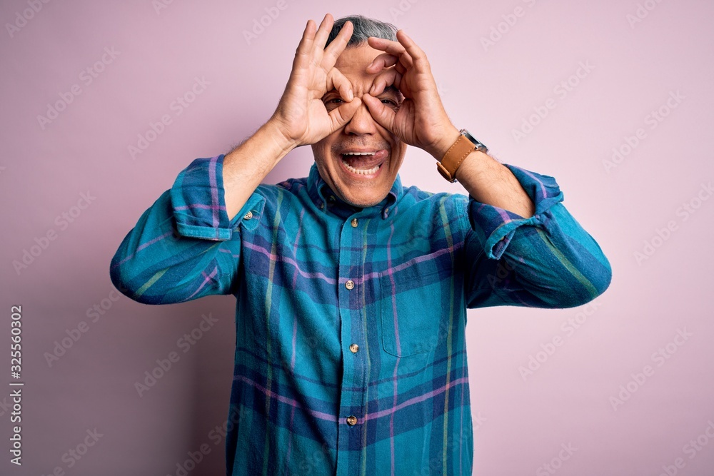 Middle age handsome grey-haired man wearing casual shirt over isolated pink background doing ok gesture like binoculars sticking tongue out, eyes looking through fingers. Crazy expression. Middle age handsome grey-haired man wearing casual shirt over isolated pink background doing ok gesture like binoculars sticking tongue out, eyes looking through fingers. Crazy expression.