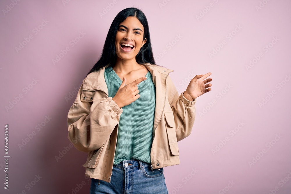 Young beautiful hispanic fashion woman wearing winter jacket and sweater over pink background smiling and looking at the camera pointing with two hands and fingers to the side. Young beautiful hispanic fashion woman wearing winter jacket and sweater over pink background smiling and looking at the camera pointing with two hands and fingers to the side.