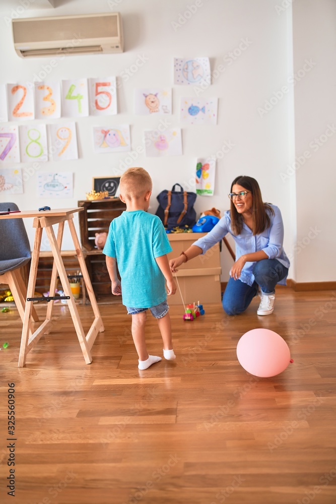 Young caucasian child playing at playschool with teacher. Mother and son at playroom around toys. Young caucasian child playing at playschool with teacher. Mother and son at playroom around toys.