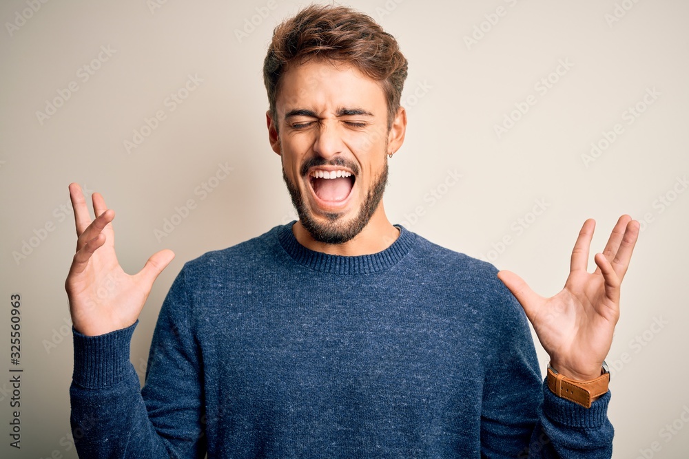 Fototapeta premium Young handsome man with beard wearing casual sweater standing over white background celebrating mad and crazy for success with arms raised and closed eyes screaming excited. Winner concept