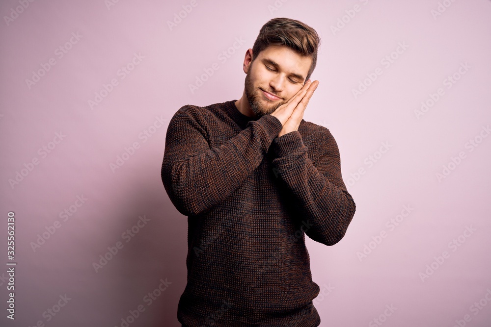 Young blond man with beard and blue eyes wearing casual sweater over pink background sleeping tired dreaming and posing with hands together while smiling with closed eyes. Young blond man with beard and blue eyes wearing casual sweater over pink background sleeping tired dreaming and posing with hands together while smiling with closed eyes.