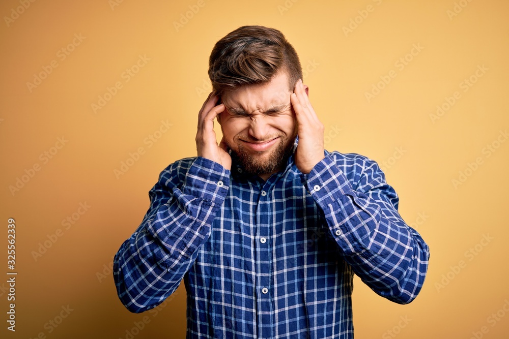 Young blond businessman with beard and blue eyes wearing shirt over yellow background with hand on headache because stress. Suffering migraine. Young blond businessman with beard and blue eyes wearing shirt over yellow background with hand on headache because stress. Suffering migraine.