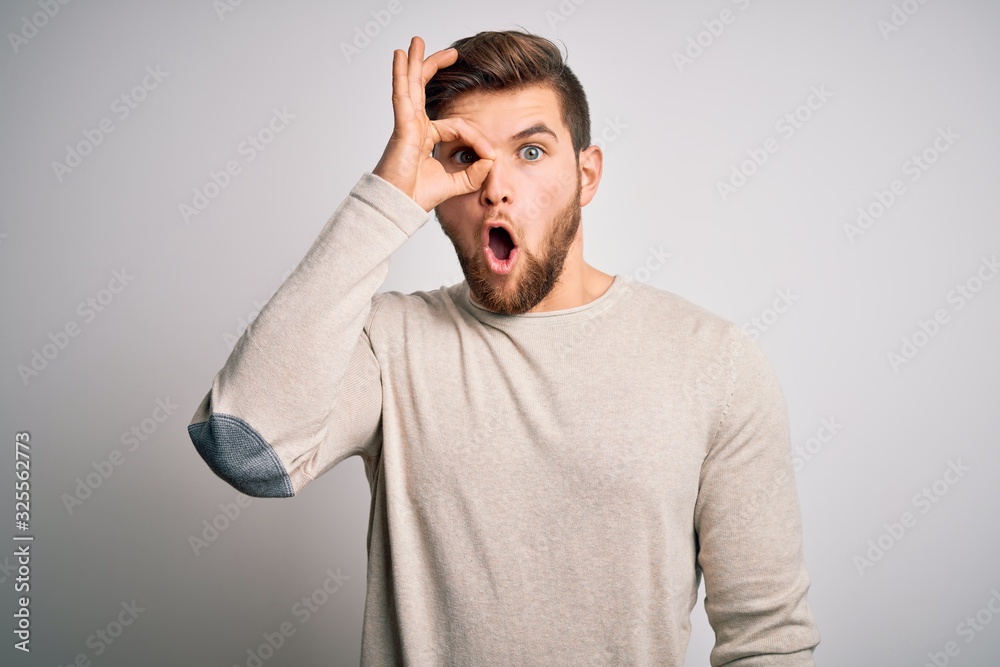Young handsome blond man with beard and blue eyes wearing casual sweater doing ok gesture shocked with surprised face, eye looking through fingers. Unbelieving expression. Young handsome blond man with beard and blue eyes wearing casual sweater doing ok gesture shocked with surprised face, eye looking through fingers. Unbelieving expression.