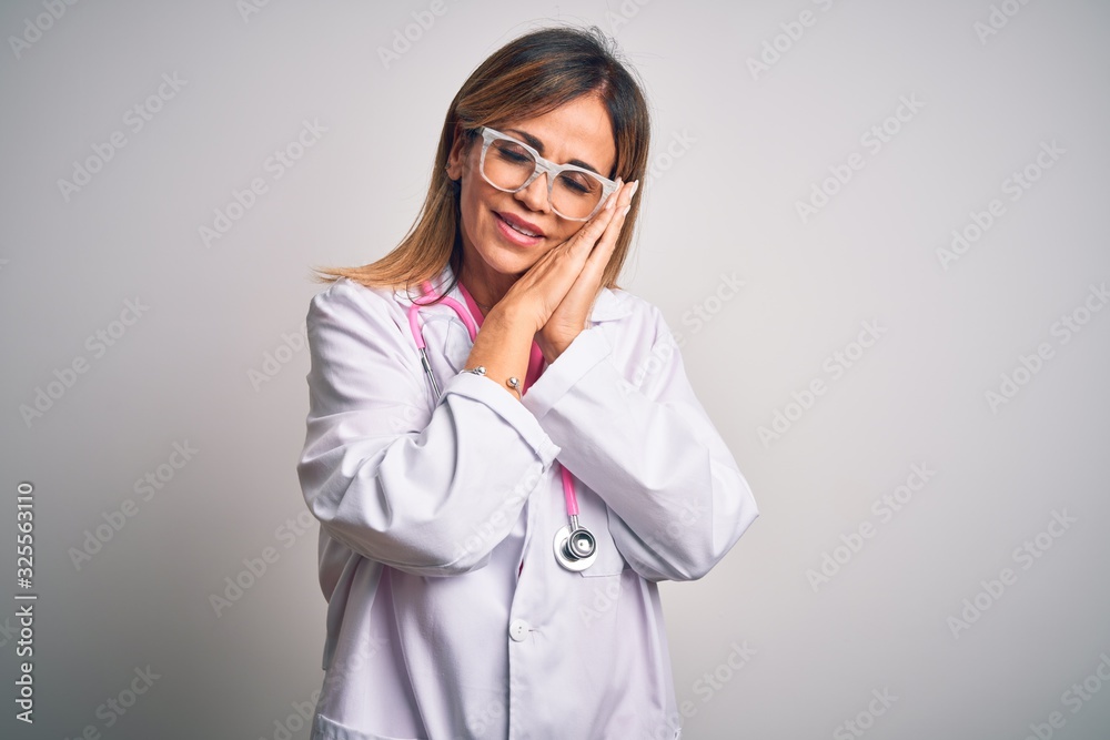 Middle age beautiful doctor woman wearing pink stethoscope over isolated white background sleeping tired dreaming and posing with hands together while smiling with closed eyes.