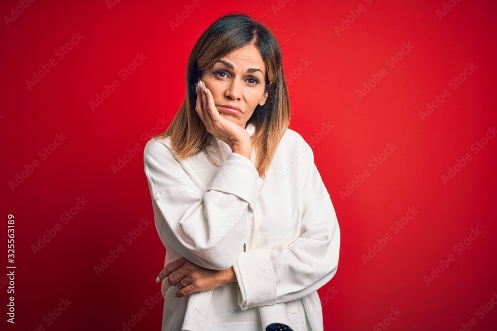 Middle age beautiful sportswoman wearing casual sweatshirt over isolated red background thinking looking tired and bored with depression problems with crossed arms. Middle age beautiful sportswoman wearing casual sweatshirt over isolated red background thinking looking tired and bored with depression problems with crossed arms.