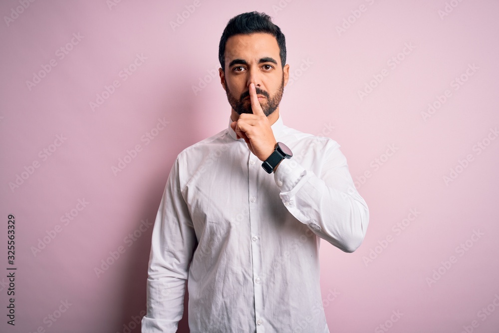 Young handsome man with beard wearing casual shirt standing over pink background asking to be quiet with finger on lips. Silence and secret concept. Young handsome man with beard wearing casual shirt standing over pink background asking to be quiet with finger on lips. Silence and secret concept.