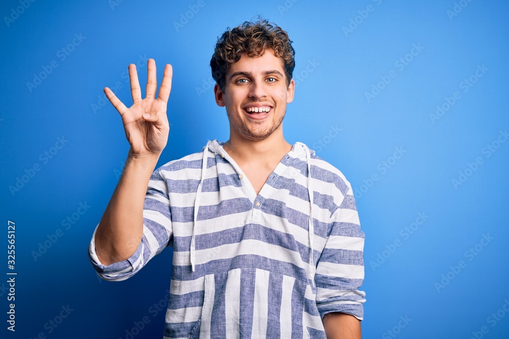 Young blond handsome man with curly hair wearing casual striped sweatshirt showing and pointing up with fingers number four while smiling confident and happy. Young blond handsome man with curly hair wearing casual striped sweatshirt showing and pointing up with fingers number four while smiling confident and happy.