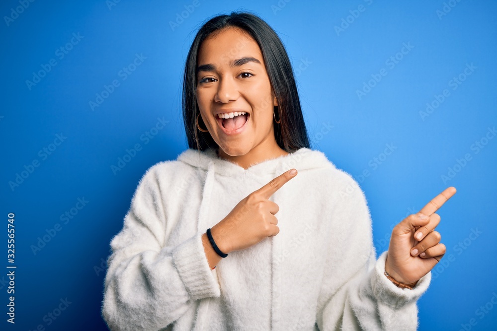 Young beautiful asian sportswoman wearing sweatshirt standing over isolated blue background smiling and looking at the camera pointing with two hands and fingers to the side. Young beautiful asian sportswoman wearing sweatshirt standing over isolated blue background smiling and looking at the camera pointing with two hands and fingers to the side.