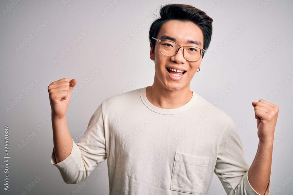 Young handsome chinese man wearing casual t-shirt and glasses over white background celebrating surprised and amazed for success with arms raised and open eyes. Winner concept. Young handsome chinese man wearing casual t-shirt and glasses over white background celebrating surprised and amazed for success with arms raised and open eyes. Winner concept.