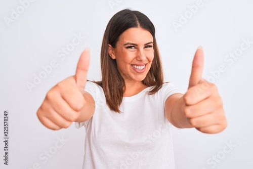 Portrait of beautiful and young brunette woman standing over isolated white background approving doing positive gesture with hand, thumbs up smiling and happy for success. Winner gesture. © Krakenimages.com