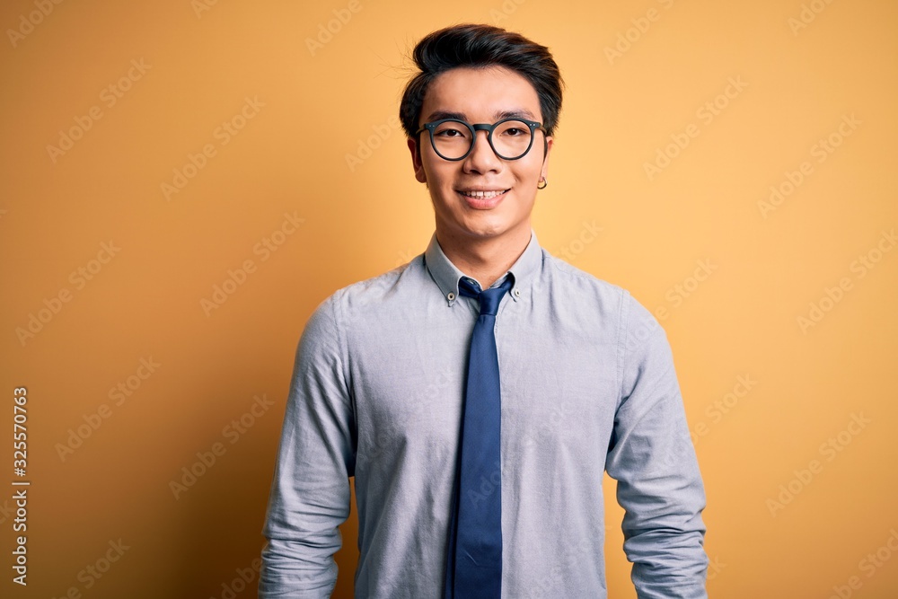 Young handsome chinese businessman wearing glasses and tie over yellow background with a happy and cool smile on face. Lucky person. Young handsome chinese businessman wearing glasses and tie over yellow background with a happy and cool smile on face. Lucky person.