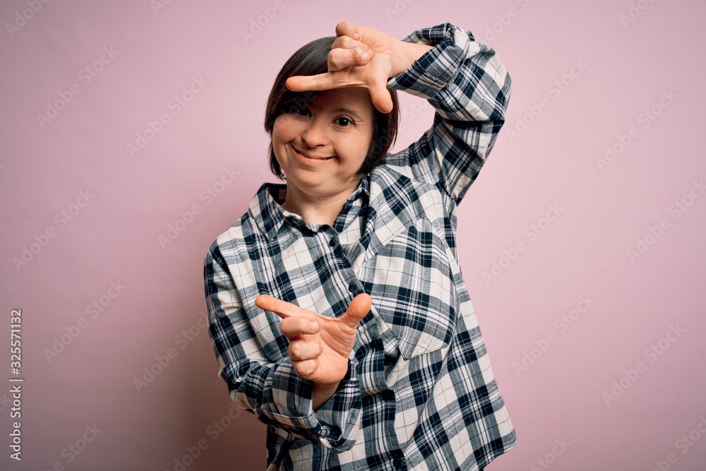 Young down syndrome woman wearing casual shirt over pink background smiling making frame with hands and fingers with happy face. Creativity and photography concept. Young down syndrome woman wearing casual shirt over pink background smiling making frame with hands and fingers with happy face. Creativity and photography concept.