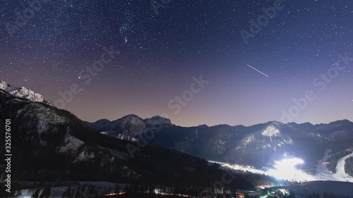 All night timelapse of the night sky and the valley near San Vigilio, Northern Italy. The sky is full of stars, the valley is aglow with lights from night skiing, pisten bullies and cars. photo