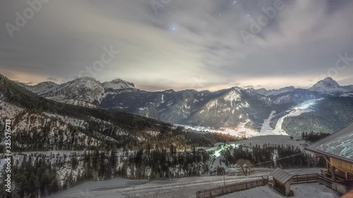 A full night timelapse of the sky and the valley near the town of Al Plan in South Tyrol, Italy. Clouds flying over the night sky, pisten bullies moving on the slopes, the town is aglow with lights. photo