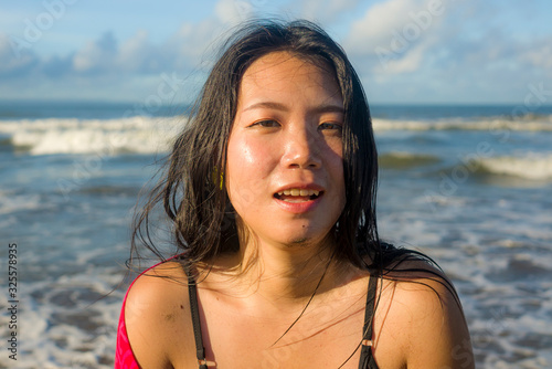 outdoors lifestyle portrait of young beautiful and happy Asian Korean woman in swimsuit at the beach playing carefree with sarong enjoying Summer holiday feeling free and blissful