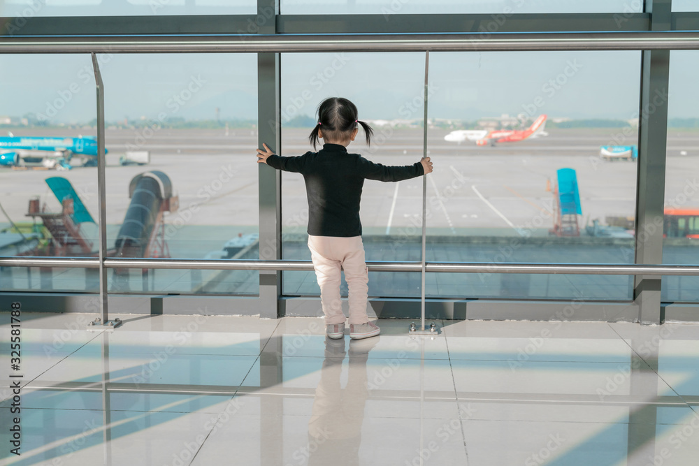 Little Asian baby girl stands at hall and looking at airplanes at the airport