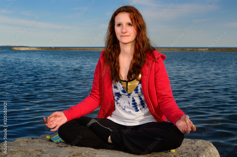 Teenage girl on rock by Lake Ontario meditating in yoga lotus position