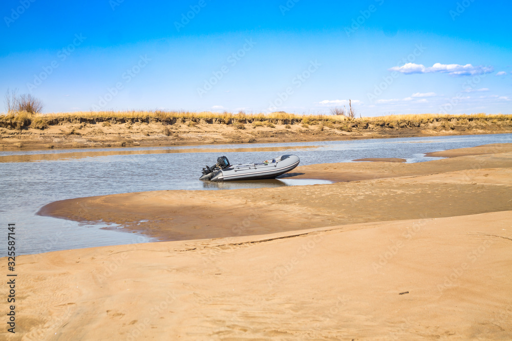 River motor boat near sandy river bank with golden dunes and blue water River motor boat near sandy river bank with golden dunes and blue water