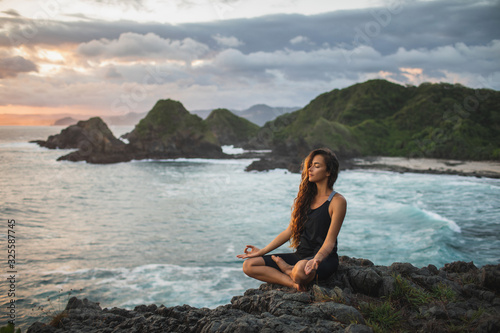 Young woman practicing yoga in lotus pose at sunset with beautiful ocean and mountain view. Sensitivity to nature. Self-analysis and soul-searching. Spiritual and emotional concept. © Oleg Breslavtsev