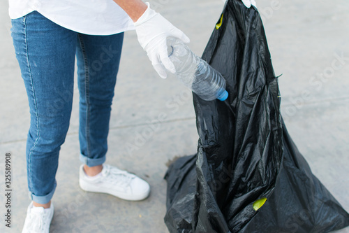Woman in white globes puting plastic bottle in trash bag