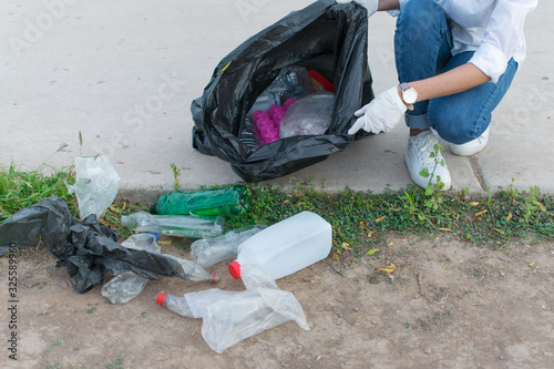 Woman in white globes puting plastic bottle in trash bag