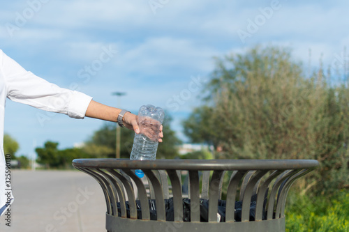Person putting plastic bottle inside trash can