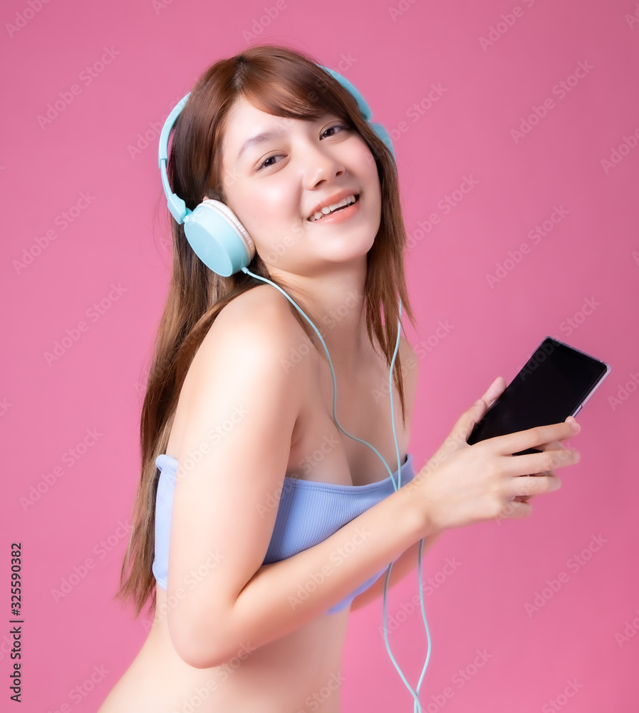 Asian young girl in colorful bikini  posing with smile and laughing.  Teenage female model in headphones having fun in summer studio photoshoot pink background.