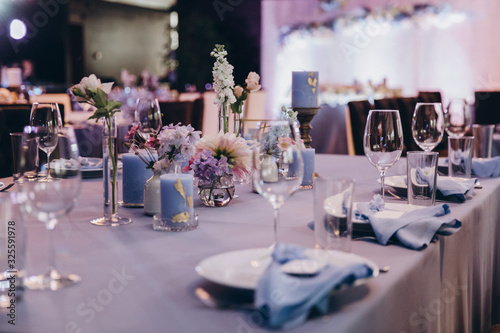 the festive table at the wedding party is decorated with flower arrangements  on the table are plates with napkins  glasses  candles  cutlery