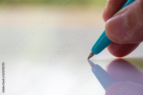 Woman's right Hand holding  blue plastic ballpoint pen, Writing letter on white acrylic background, Close up & Macro shot, Selective focus, Communication, Business, Education, Stationery concept