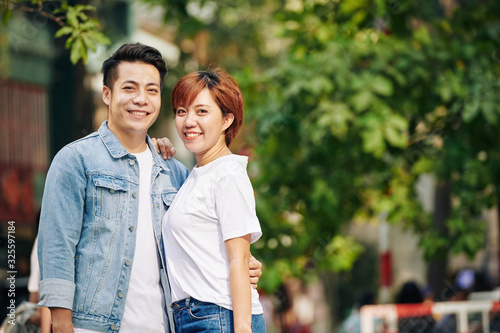 Portrait of smiling young Vietnamese couple in casual clothes hugging and looking at camera