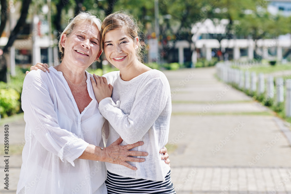 Portrait of positive mother and daughter in white clothes hugging, smiling and looking at camera Portrait of positive mother and daughter in white clothes hugging, smiling and looking at camera