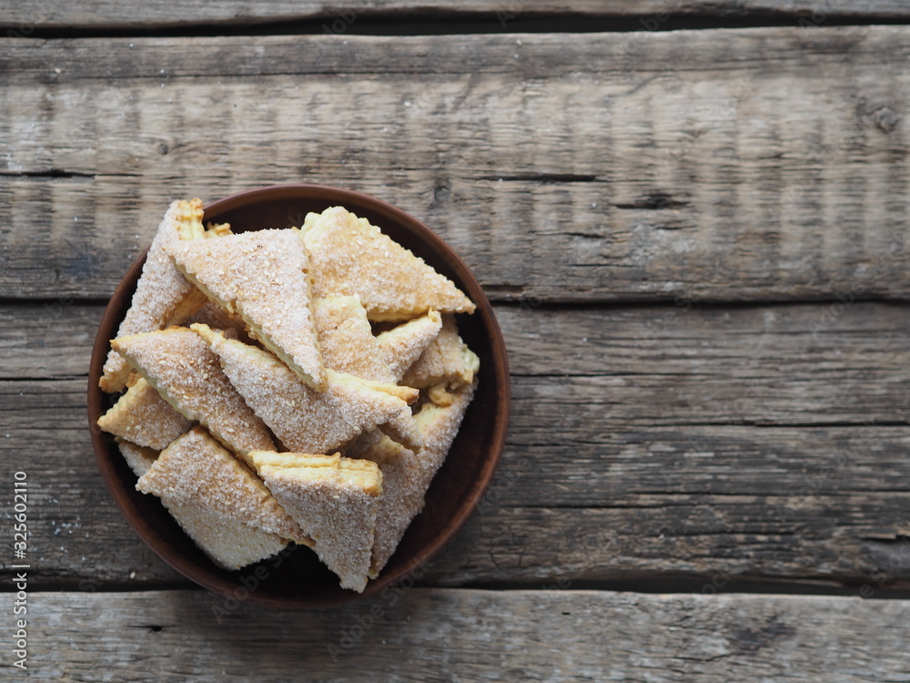 Homemade shortbread puff pastry triangle in a brown plate on a wooden ancient background. Top view. Place for text. Homemade shortbread puff pastry triangle in a brown plate on a wooden ancient background. Top view. Place for text.