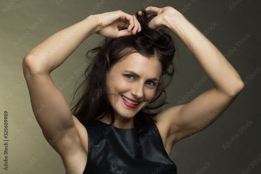 a brunette in a black leather sleeveless blouse poses on a gray background a brunette in a black leather sleeveless blouse poses on a gray background