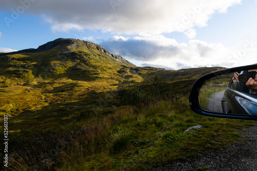 Travelers take pictures of a landscape of Norwegian mountains from their car through opened windows. They are reflected in a rear-view mirror of the car. Travel distinations. photo