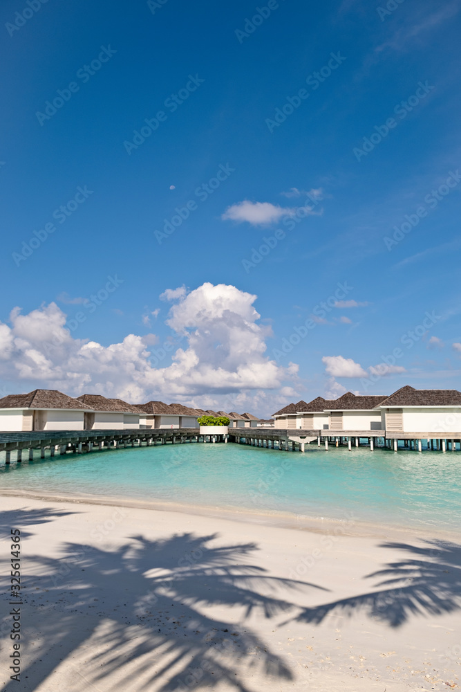 Ocean water villas and wooden jetty with the bright blue sky and the crystal clear sea water of Maldives, vertical composition