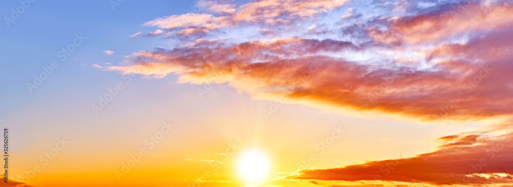 sunset sky landscape background natural color of evening cloudscape with setting sun. Orange clouds against blue and yellow sky. Colorful panorama wallpaper. Ultra wide panoramic view. Banner template