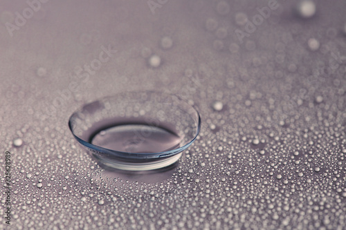 Contact lens and water drops on grey background