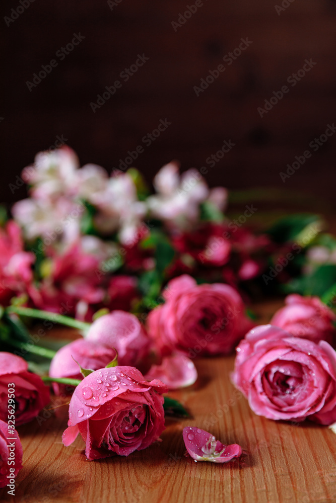 Fresh pink roses flowers with petals an leaves on the wooden table and dark black background. Still life. Copy space