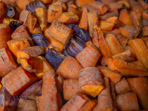 Close up of a tray of oven roasted carrots and red onion covered in an aromatic spice powder