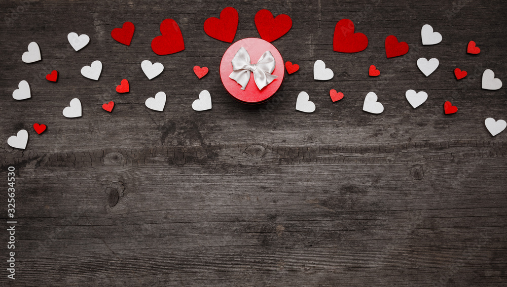 Obraz premium A small round red gift box with a bow on a dark wooden background. Place for text