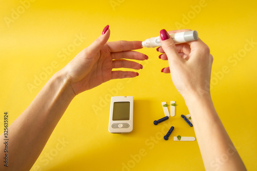 Diabet. Medical equipment. Medical concept. Close up of woman hands on yellow background using lancet on finger to check blood sugar level by Glucose meter 