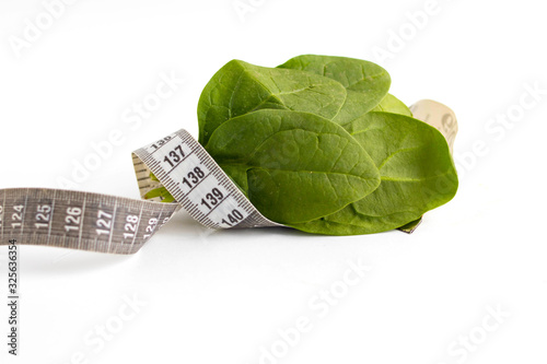 Fresh spinach leaves and measuring tape on a white background. The concept of healthy eating and weight loss.