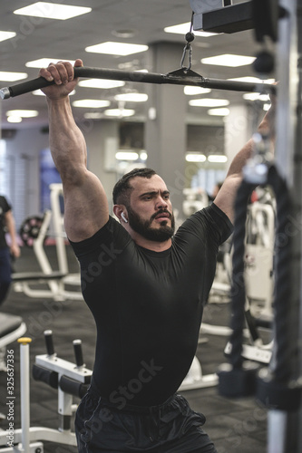 heavy weight lifting training in sport gym by young bearded man in black shirt and wireless headset pumping iron with effort