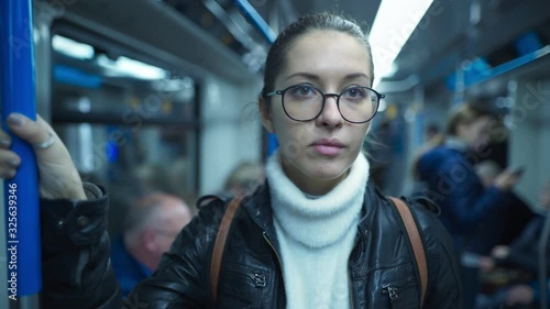 Portrait of Woman standing on a subway train while holding on to a pole