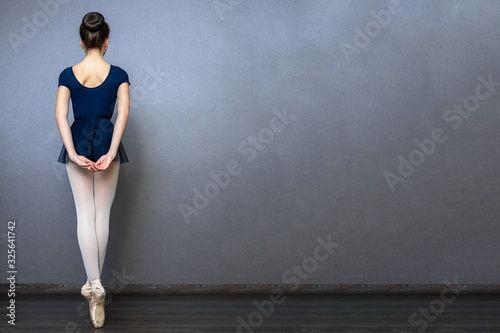 Young beautiful ballet dancer in short dress is posing in studio with a dark background. Copy space. Back view.