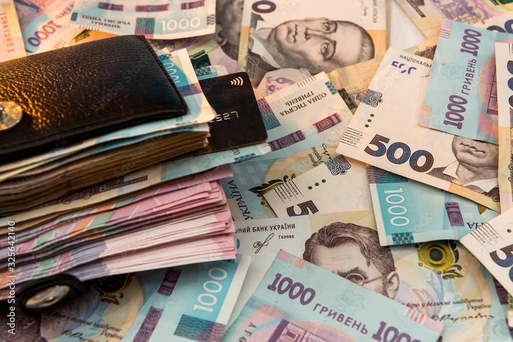 The thick money-laden black men's wallet lies against the backdrop of Ukrainian hryvnia money.