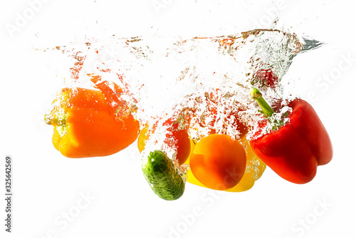 Peppers, tomato and cucumber fall into the water with splashes, isolated on a white background.