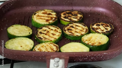 slices of zucchini languish in a grill pan. There is smoke from frying zucchini on a hot oil pan.