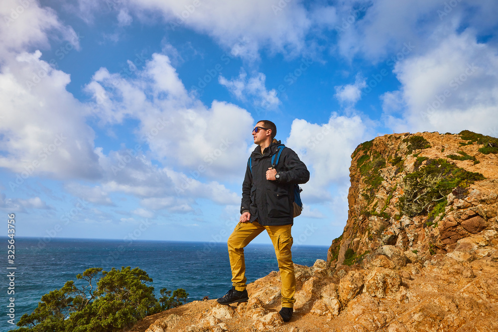 Young man tourist at Cape Cabo da Roca with view on beautiful landscape, winter trip . Westernmost point of Europe in Portugal Young man tourist at Cape Cabo da Roca with view on beautiful landscape, winter trip . Westernmost point of Europe in Portugal
